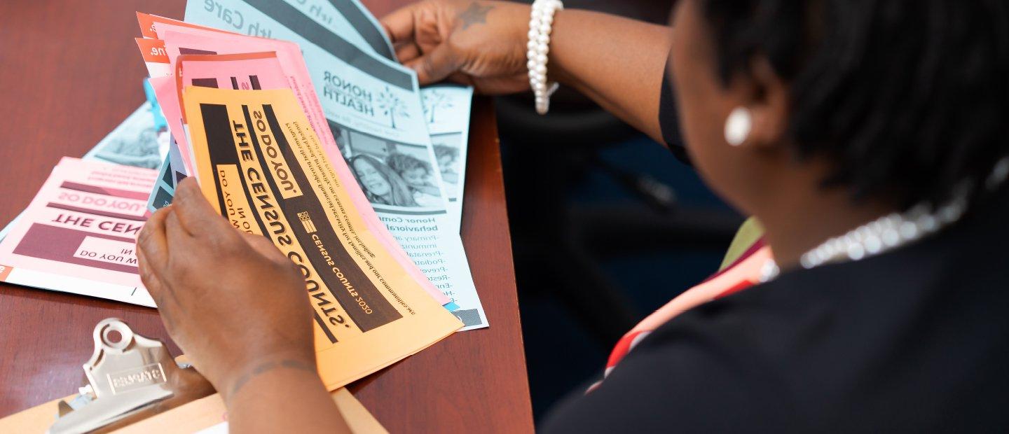 A woman seated at a table, looking through Census and health care flyers.